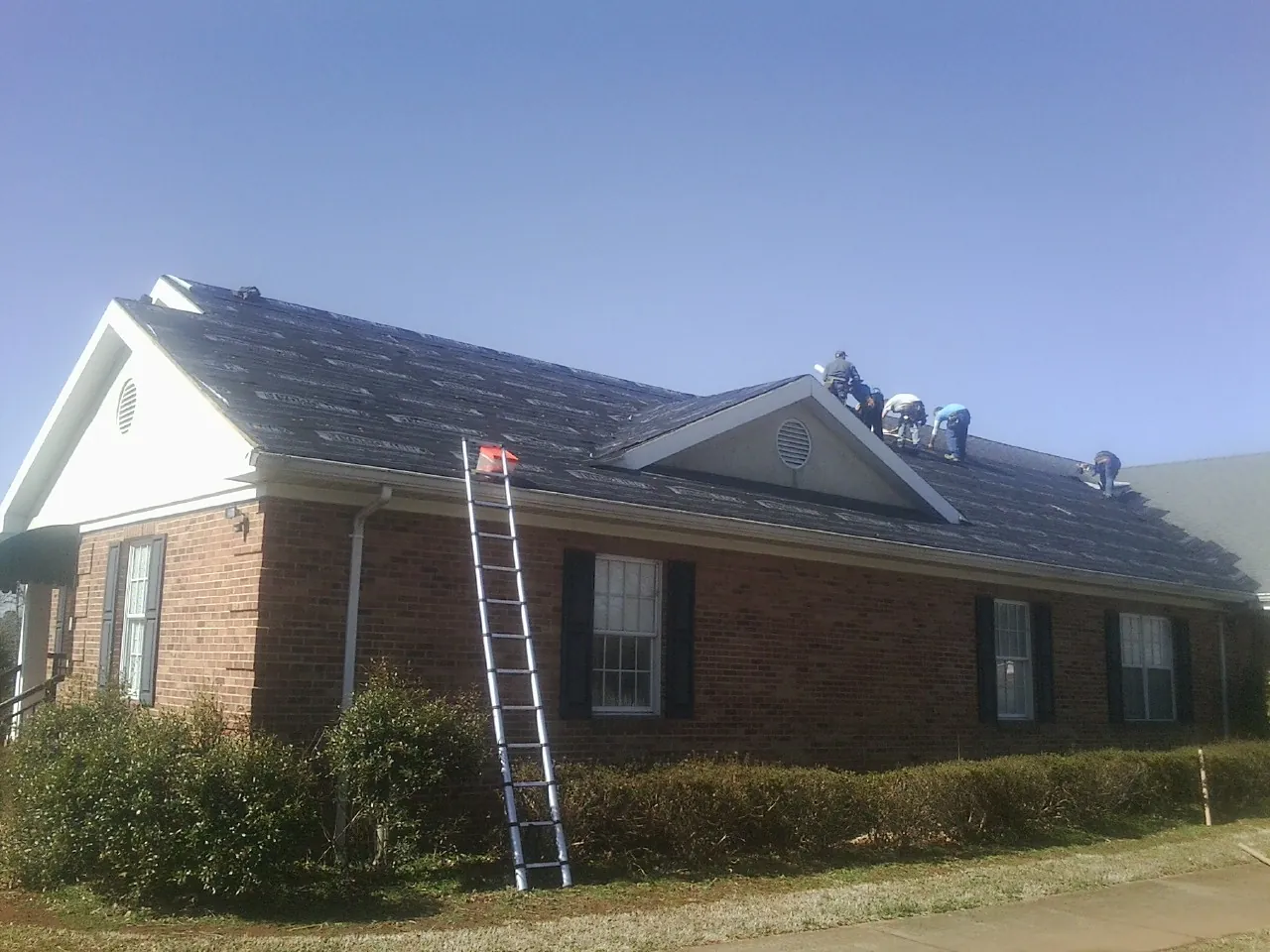 Crew tearing shingles off a brick ranch roof with a ladder set — Emergency Roof Repair work by our crew in Oxford