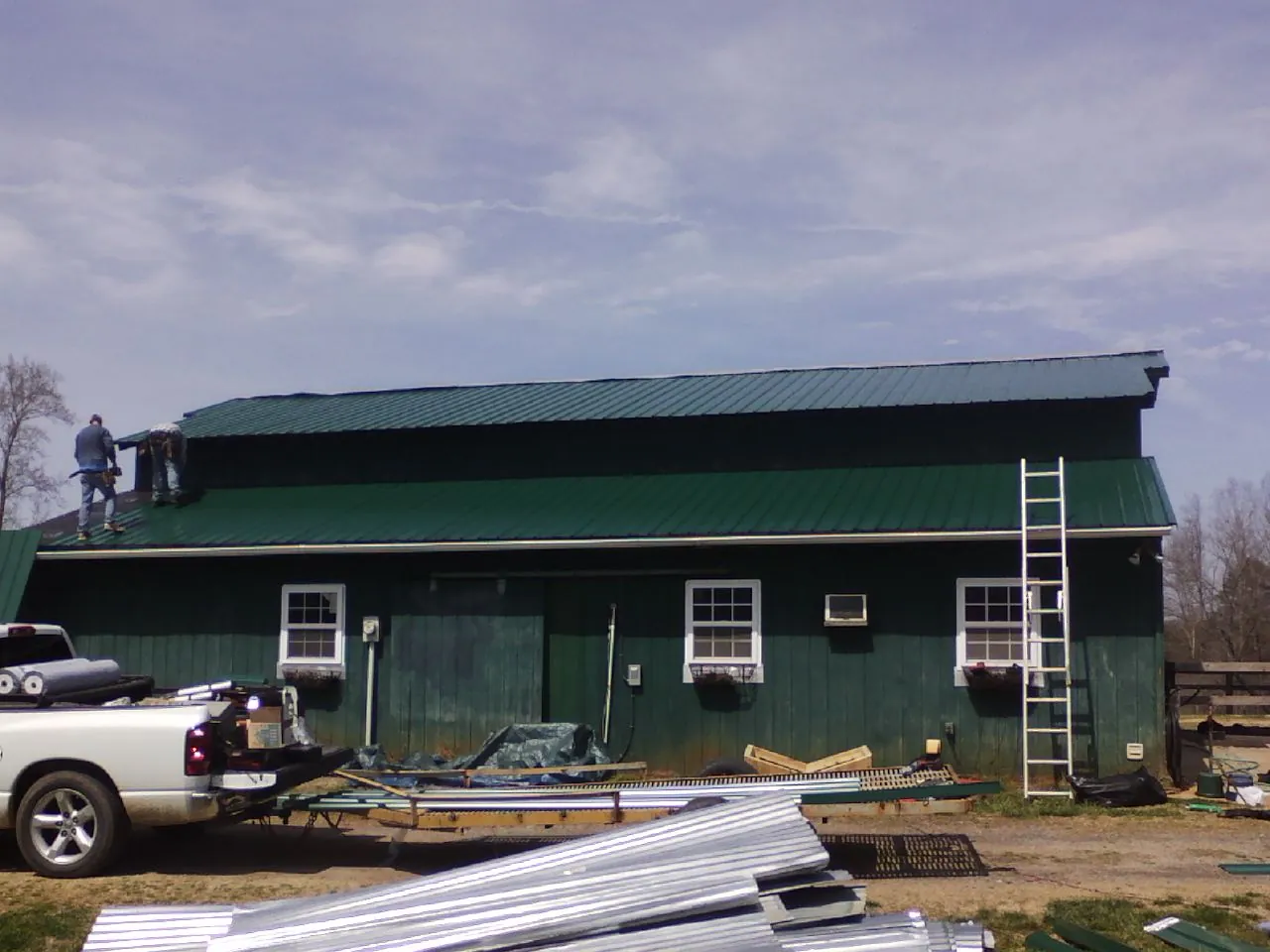 Crew installing green metal roofing on a large green barn in Oxford